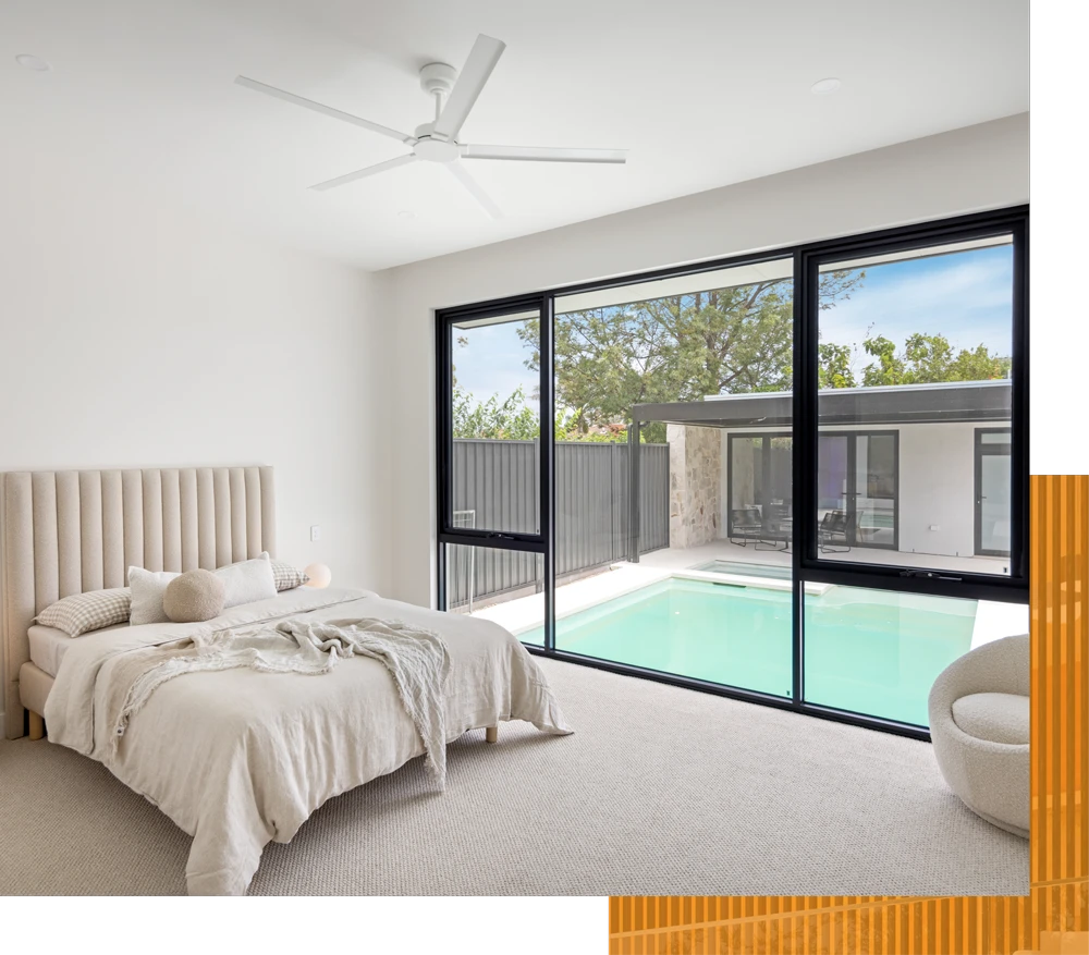 Bedroom with a view of a pool through a large window with a black frame The room has a large bed and a ceiling fan.